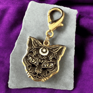 Metal keychain with a triple-eyed cat design on a stone slab.