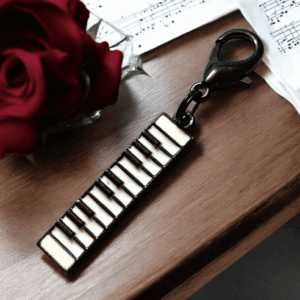 A piano keyboard keychain and a red rose on a wooden surface with sheet music.