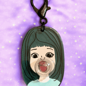 A keychain featuring a cartoon girl with green hair and a pacifier.