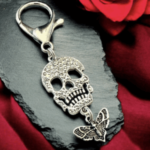 Silver skull keychain with butterfly detail on black slate and red roses.