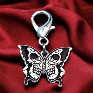 Silver butterfly charm with skull details on red fabric.