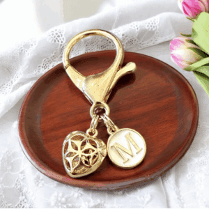Gold keychain with a heart and initial charm on a wooden dish.