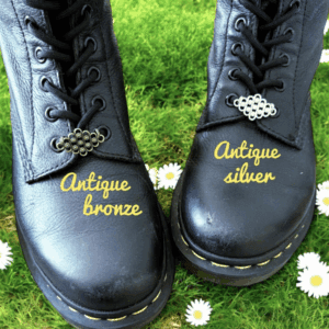 Two boots labeled Antique bronze and Antique silver on grass with daisies.