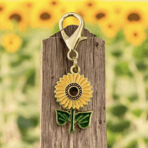 A sunflower keychain hanging on a wooden board with a sunflower backdrop.