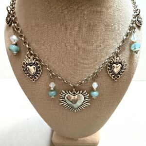 Silver heart-shaped necklace with blue beads on display bust.