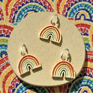 Four colorful rainbow-shaped earrings displayed on a beige surface with a vibrant background.