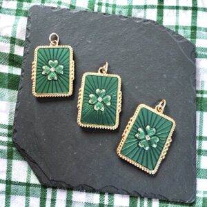 Three green and gold floral pendant charms on a dark slate.